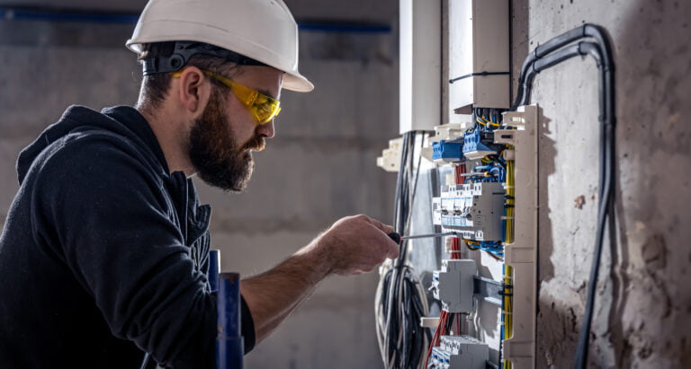 A male electrician works in a switchboard with an electrical connecting cable.